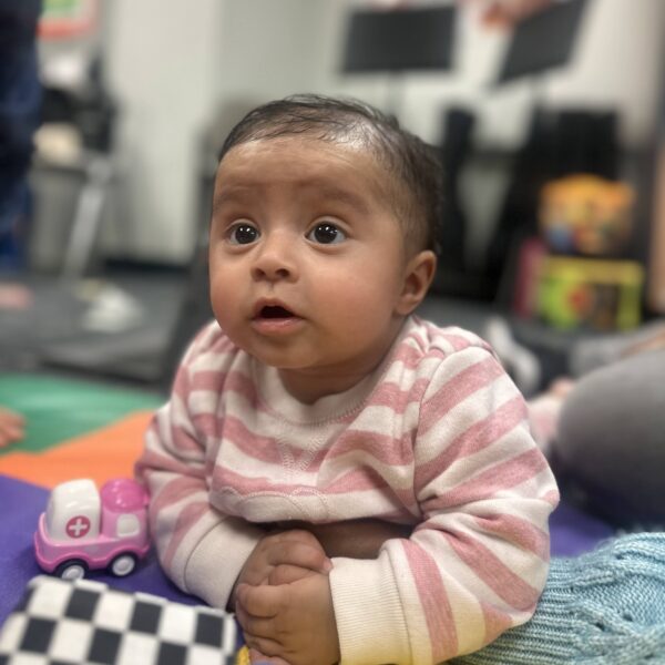 An infant wearing pink and white holds up its head.